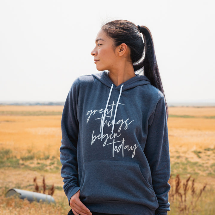 Woman wearing a unisex blue hoodie sweatshirt that says "great things begin today"