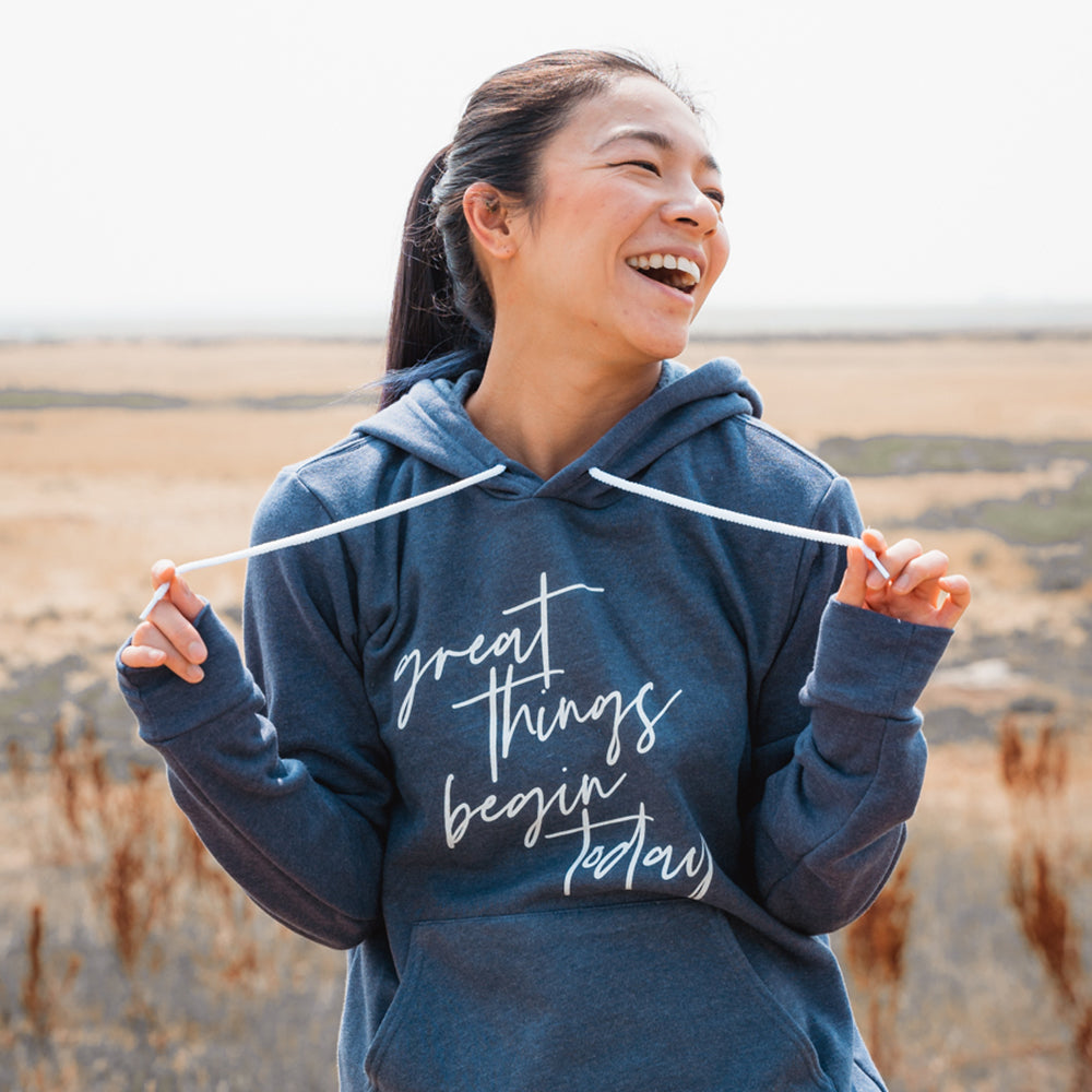 Woman wearing a unisex blue hoodie sweatshirt that says "great things begin today"