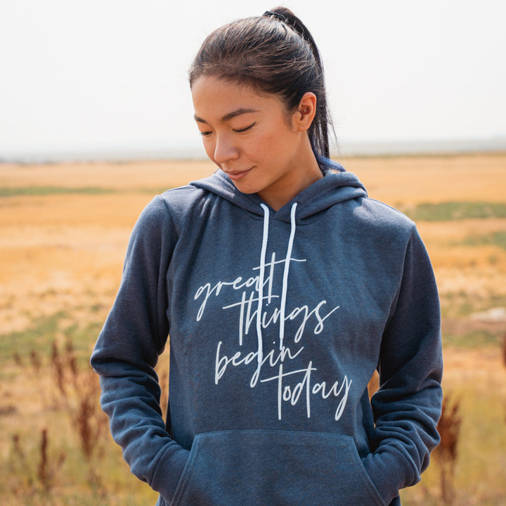 Woman wearing a unisex blue hoodie sweatshirt that says "great things begin today"