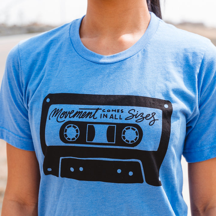 Woman wearing a heather columbia blue t-shirt that says "movement comes in all sizes"