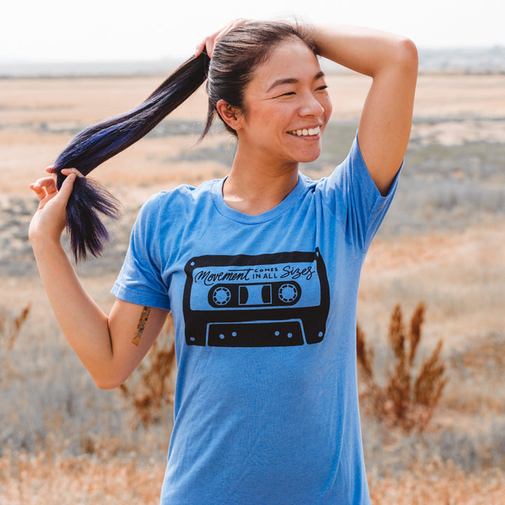 Woman wearing a heather columbia blue t-shirt that says "movement comes in all sizes"