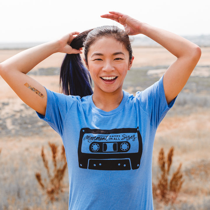 Woman wearing a heather columbia blue t-shirt that says "movement comes in all sizes"