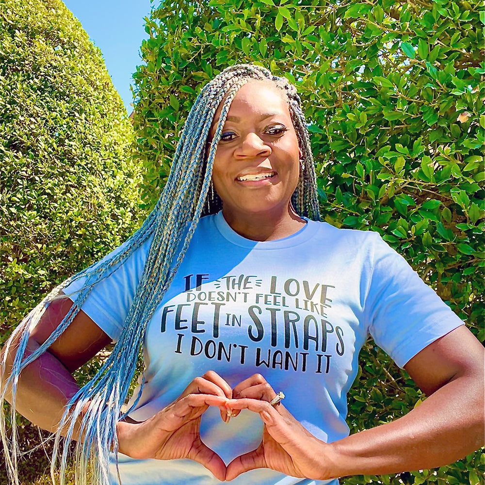 Woman wearing a unisex t-shirt that says "If the love doesn't feel like feet in straps, I don't want it". T-Shirt is from The Movement Shop.