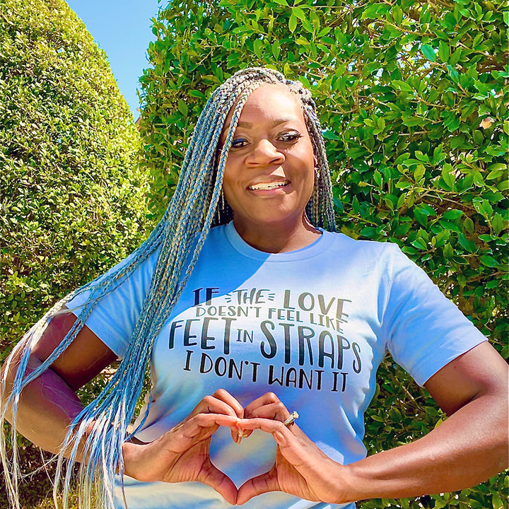 Woman wearing a unisex t-shirt that says "If the love doesn't feel like feet in straps, I don't want it". T-Shirt is from The Movement Shop.