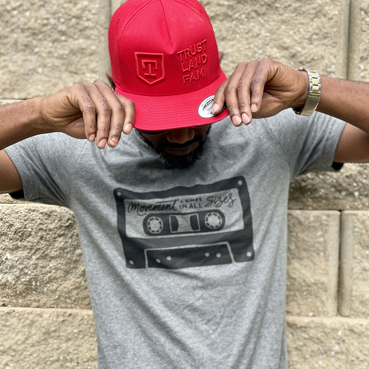 Man wearing a deep heather unisex t-shirt that says "Movement Comes In All Sizes" designed within a mixed tape