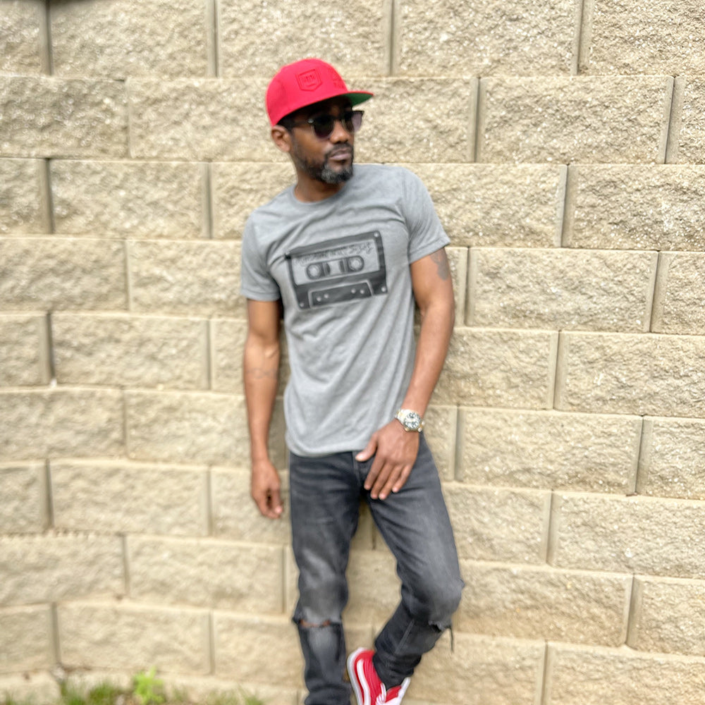 Man wearing a deep heather unisex t-shirt that says "Movement Comes In All Sizes" designed within a mixed tape