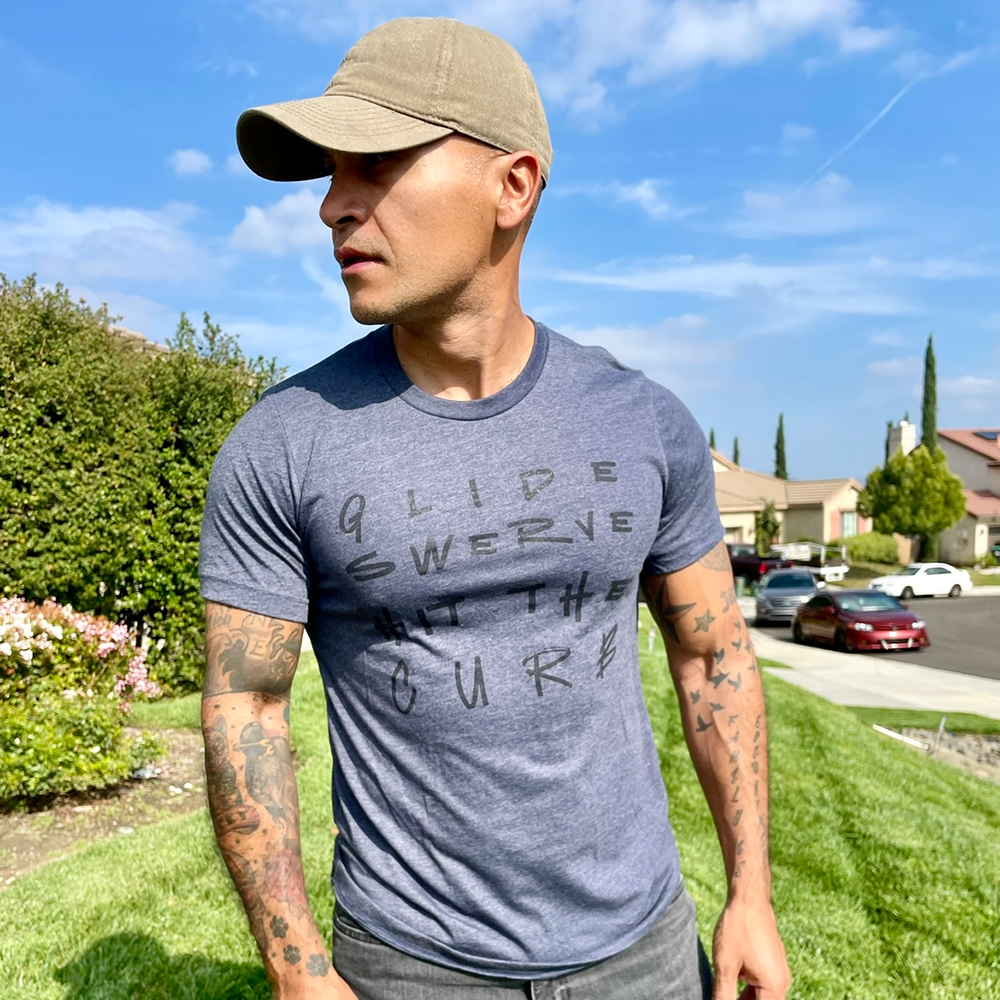 A man wearing a heather navy blue shirt that says Glide Swerve Hit The Curb, which is an ode to the song Regulators. Shirt made by The Movement Shop