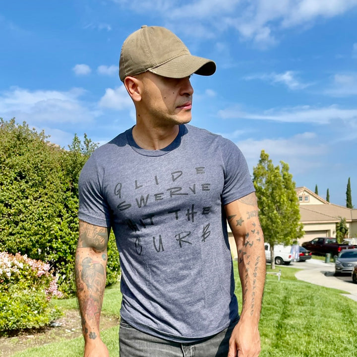 A man wearing a heather navy blue shirt that says Glide Swerve Hit The Curb, which is an ode to the song Regulators. Shirt made by The Movement Shop