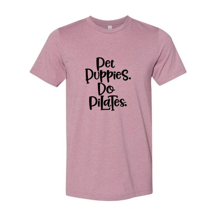 Woman wearing a unisex crewnecek Heather Orchid t-shirt that says "Pet Puppies, Do Pilats" in black text