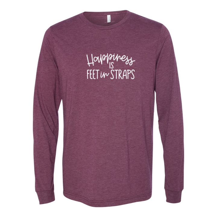 A woman wearing a long sleeve unisex crewneck long sleeve maroon triblend shirt that reads "happiness is feet in straps" in white script text
