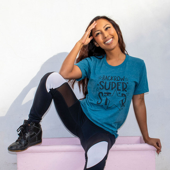 Woman in front of a white background wearing a Teal unisex crewneck t-shirt that says "Back Row Super Star"