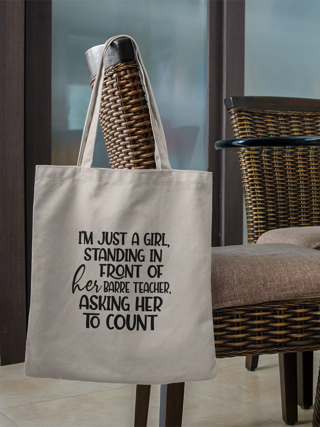 100% cotton canvas tote bag with handles that says "I'm just a girl, standing in front of her Barre Teacher, asking her to count". Bag is hanging off the back a wicker dining room chair.