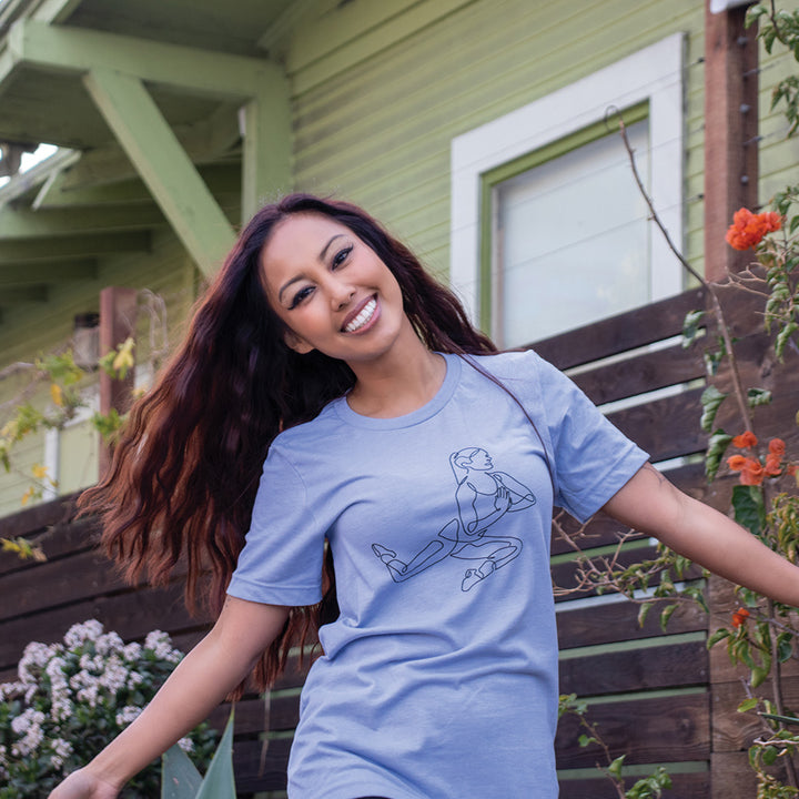 Woman wearing a heather blue t-shirt that has single line drawn woman doing the barre pretzel move.