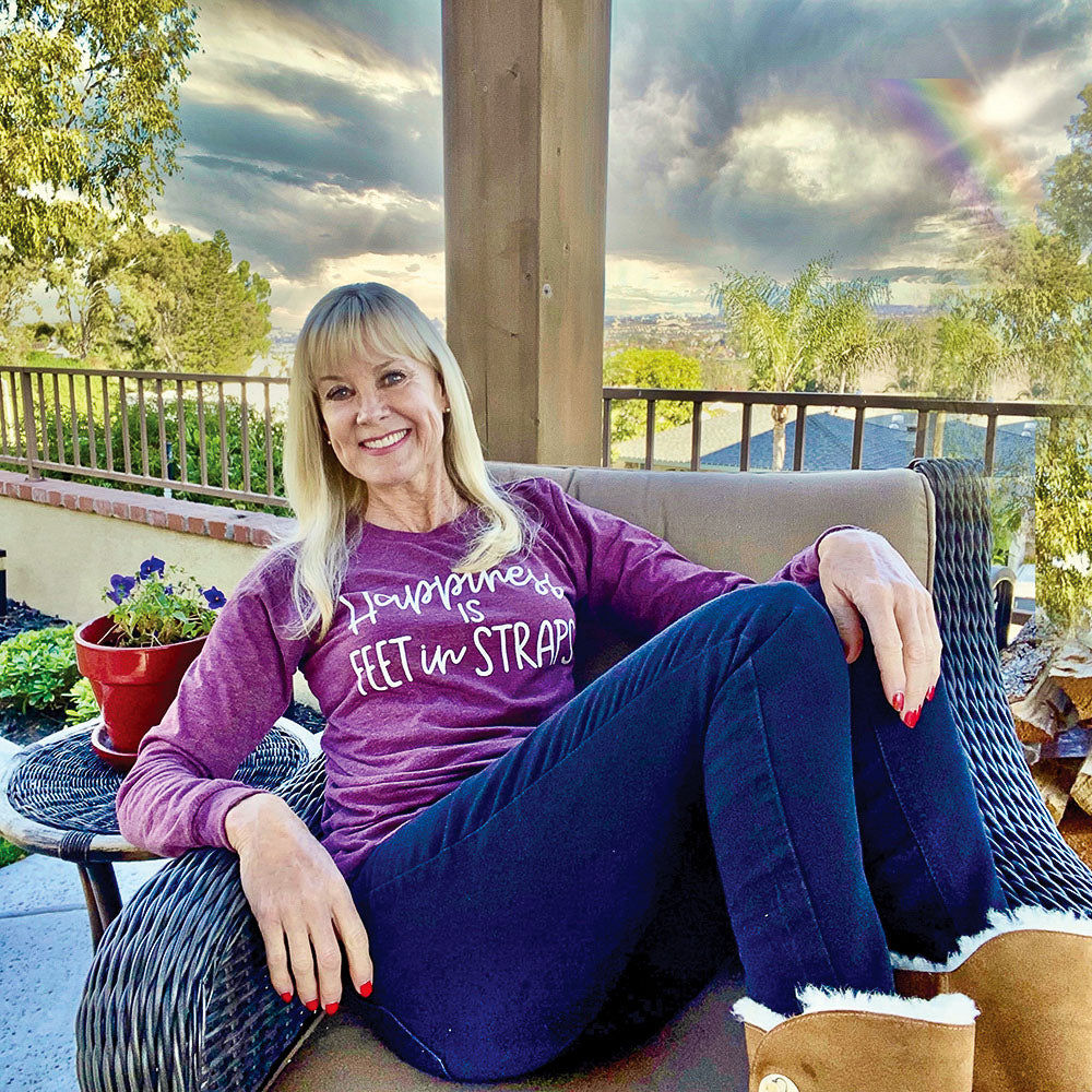 A woman wearing a long sleeve unisex crewneck long sleeve maroon triblend shirt that reads "happiness is feet in straps" in white script text