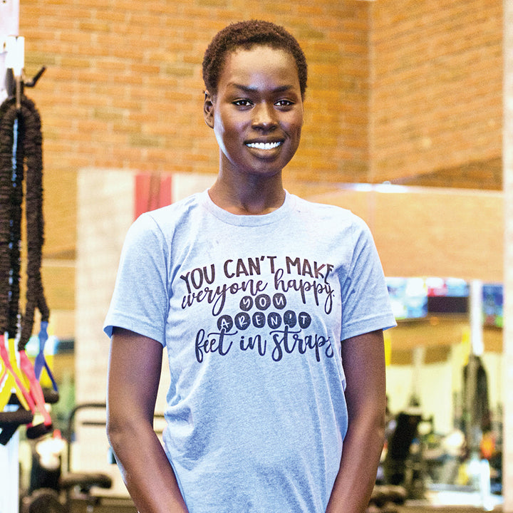Woman wearing a blue shirt that says "You can't make everyone happy, you aren't feet in straps" in black text