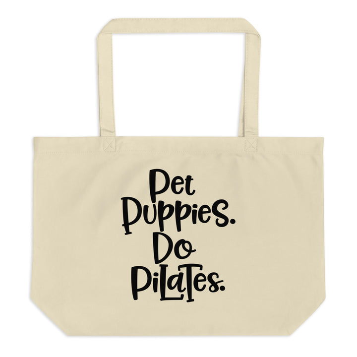 A canvas tote bag by it's handles. On the tote bag reads "Pet Puppies. Do Pilates."