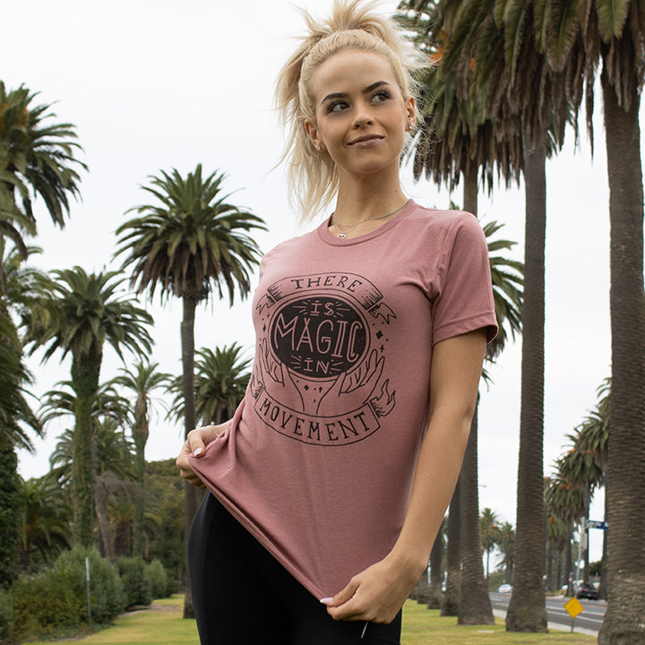 woman wearing mauve unisex crewneck t-shirt that says "There Is Magic In Movement" in black text. The words "is Magic In" is designed to look like a crystal ball.