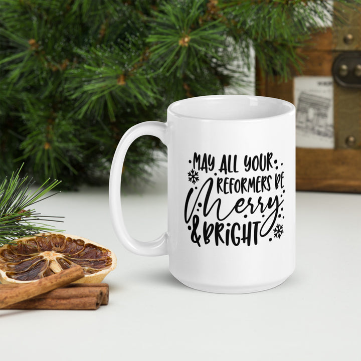 15oz white coffee mug that says "May All Your Reformers Be Merry and Bright" in Christmas style black text.