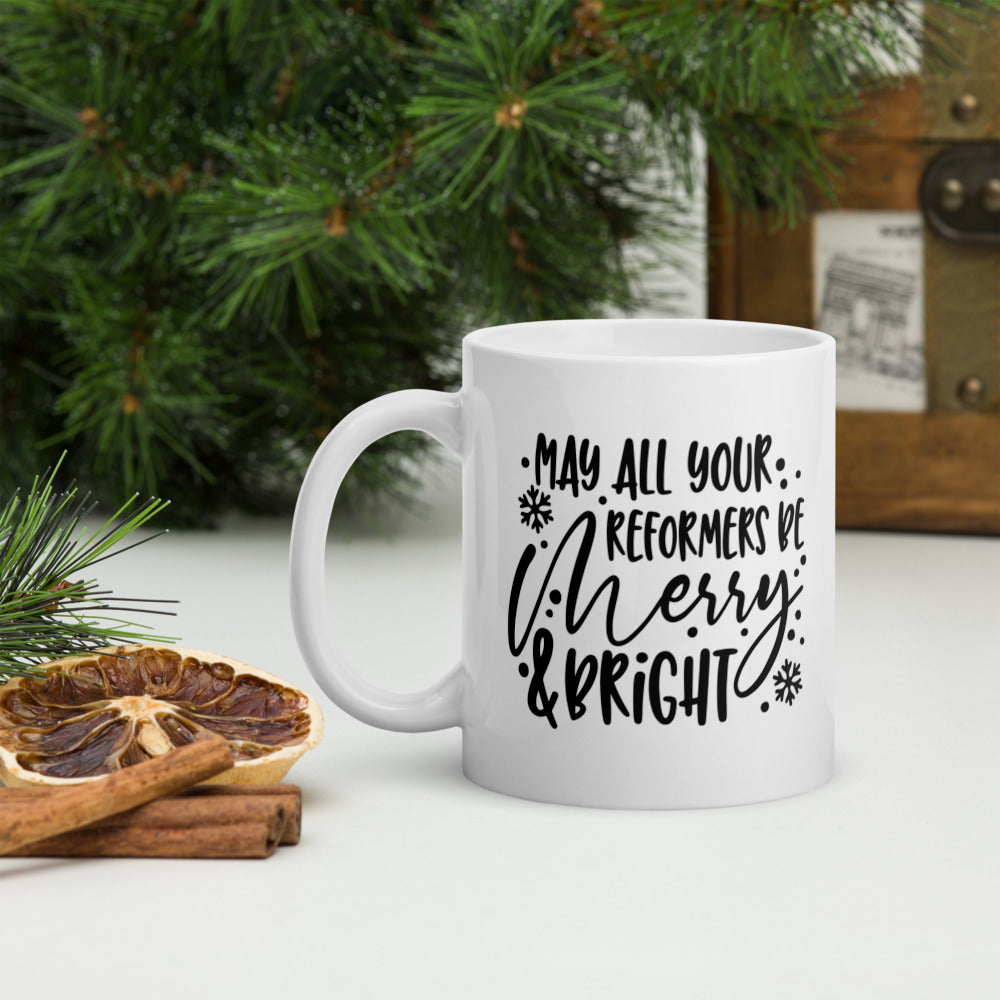 11oz white coffee mug that says "May All Your Reformers Be Merry and Bright" in Christmas style black text.