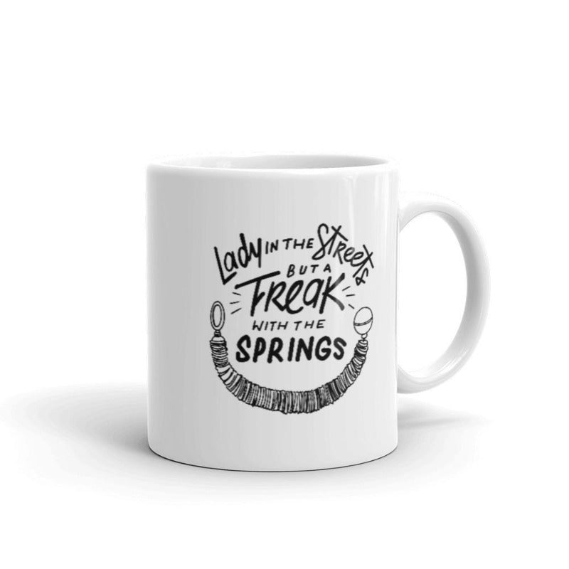 11oz Coffee Mug that says Lady In The Streets But A  Freak With The Springs. There is Pilates reformer spring under the text. Design is in black.