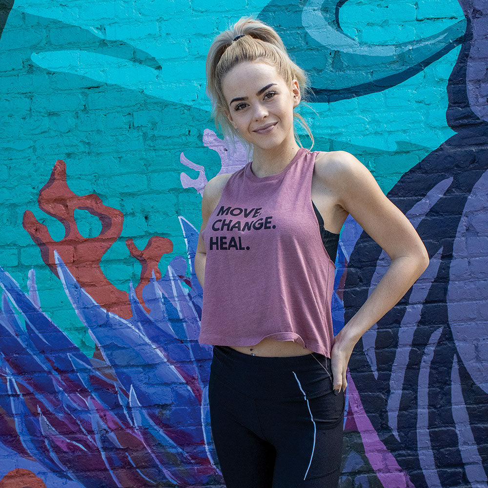 Woman wearing a mauve crop muscle tank top that says "Move. Change. Heal." in black text 