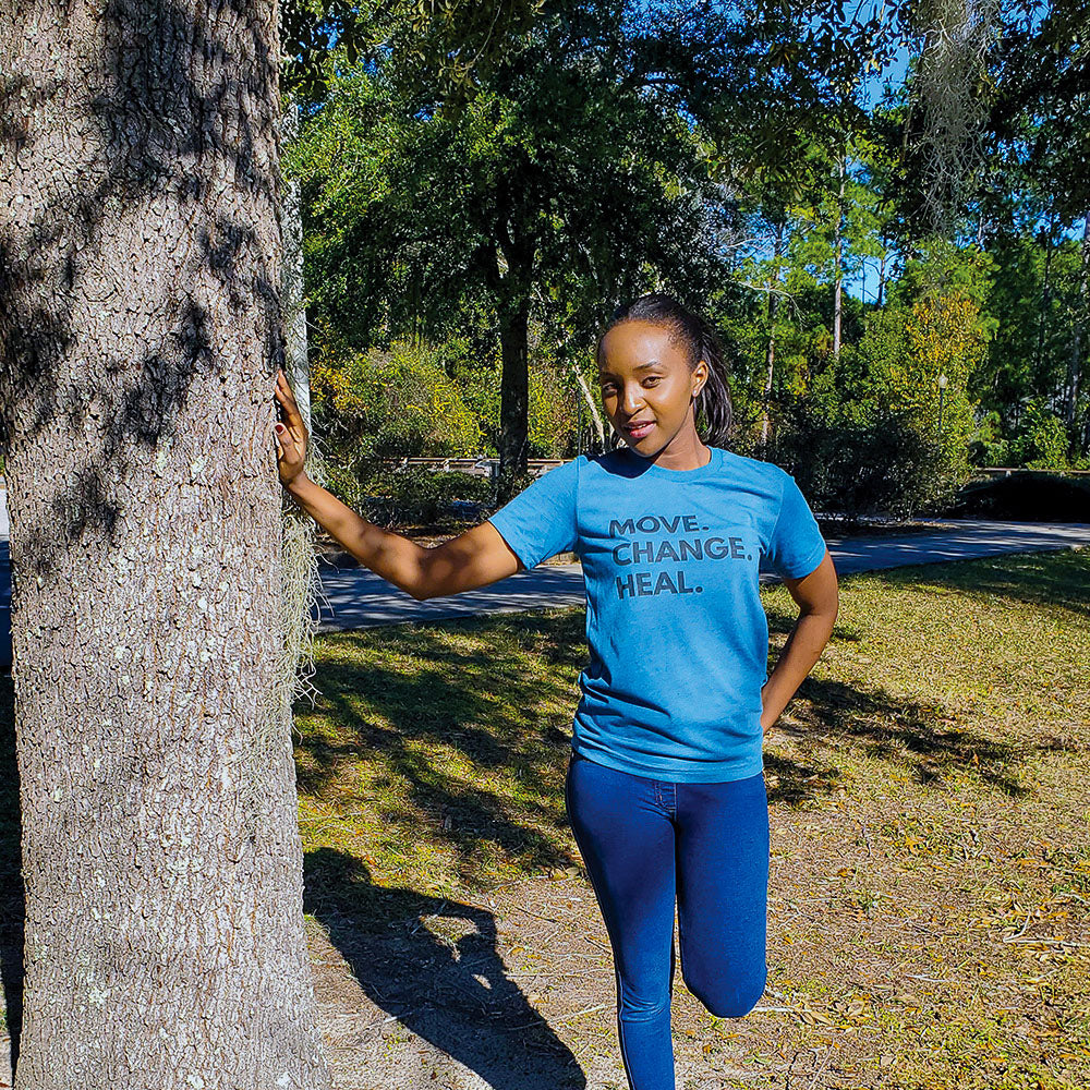 Woman leaning against a tree outside wearing a unisex crewneck t-shirt that says "Move Change Heal"