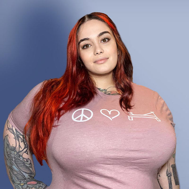 Woman wearing a unisex crew neck heather orchid t-shirt that shows a peace sign, a heart, or a pilates reformer.