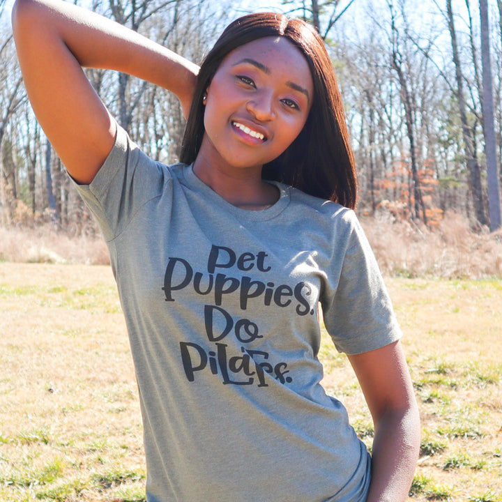 Woman wearing a unisex crewneck green t-shirt that says "Pet Puppies, Do Pilates" in black text