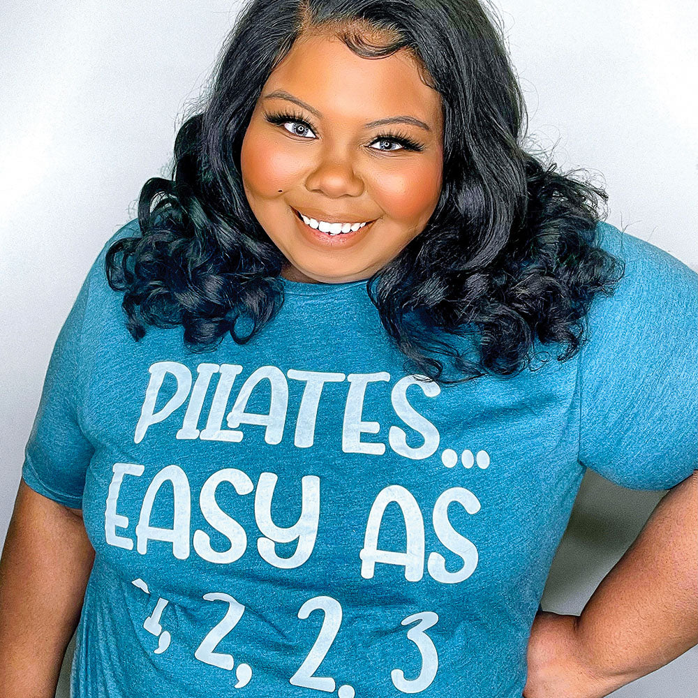 Woman wearing a heather deep teal unisex crewneck t-shirt that says "Pilates easy as 1,2,2,3" in white text