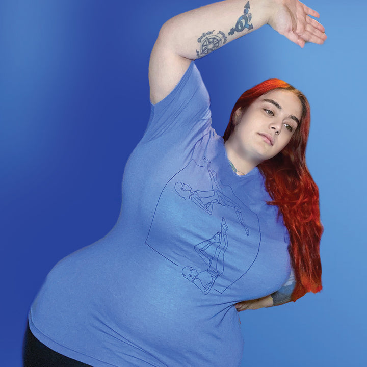 Woman wearing a heather columbia blue unisex crew t-shirt that has a line drawing of two people doing the Pilates Exercise the bicycle