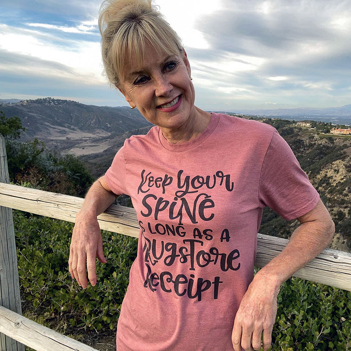 Woman wearing a mauve unisex crew neck t-shirt that says "Keep your spine as long as a drug store receipt"