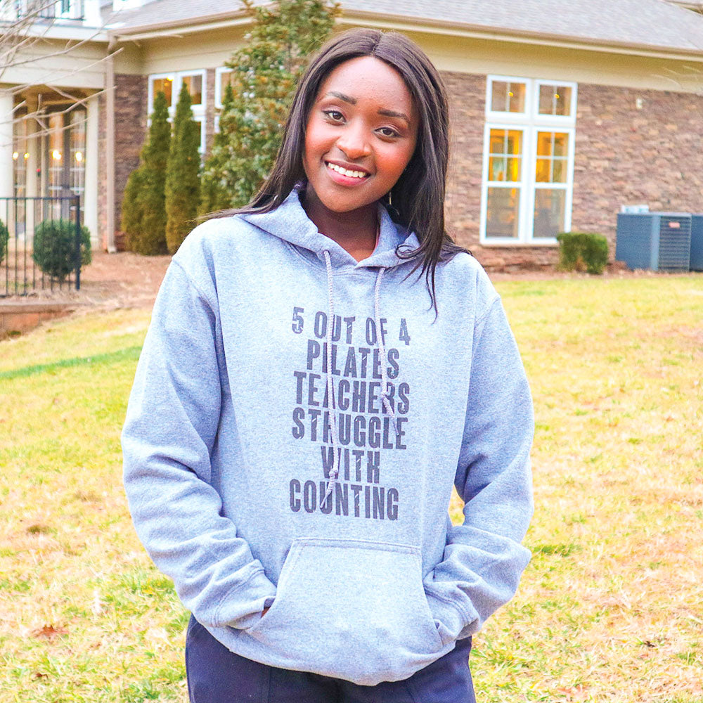 woman wearing a grey unisex hoodie with white drawcord that says "5 out of 4 Pilates Teachers Struggle With Counting"