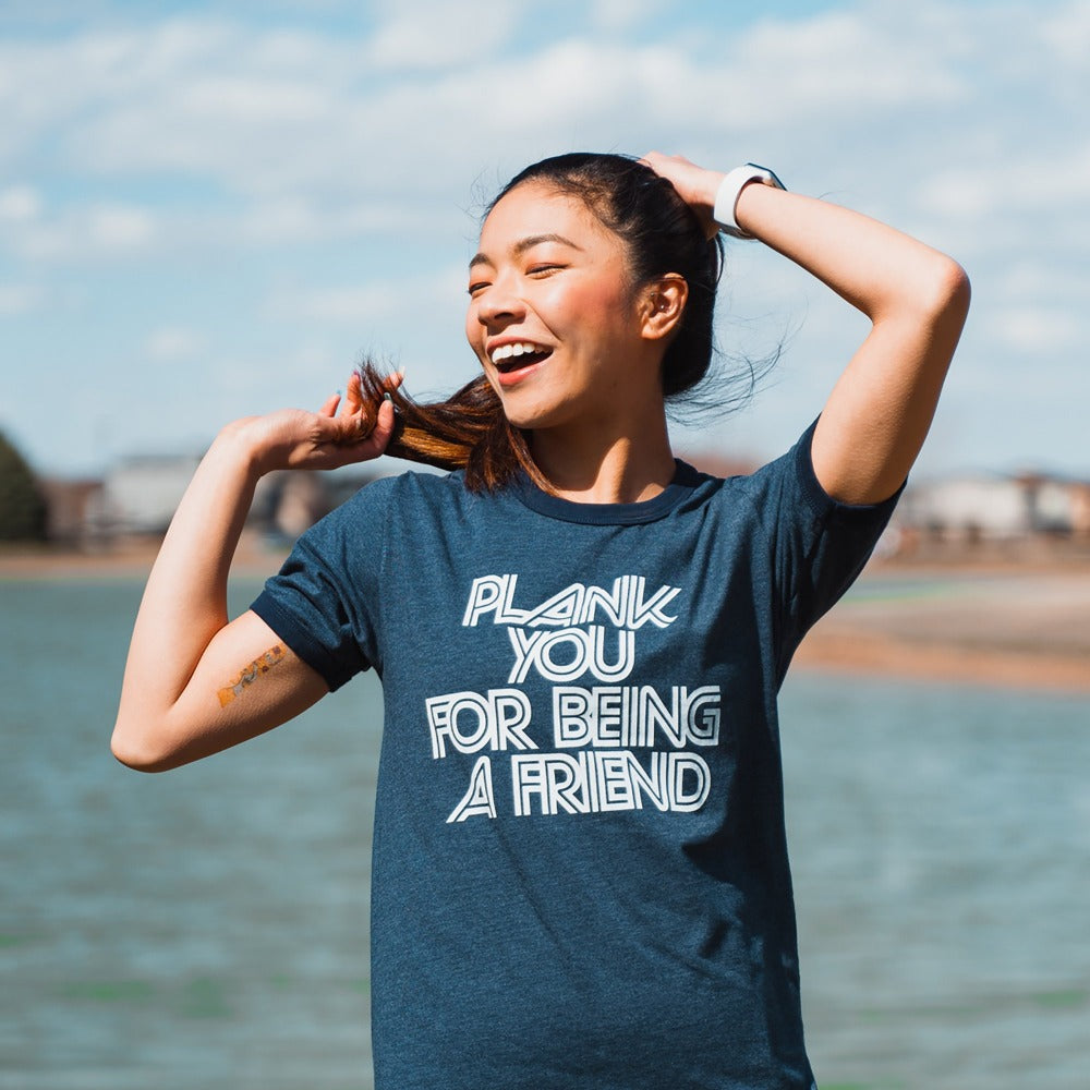 Woman wearing a blue ringer t-shirt that says "plank you for being a friend" in white writing