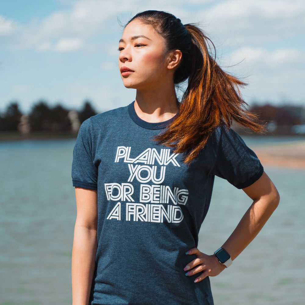 Woman wearing a blue ringer t-shirt that says "plank you for being a friend" in white writing
