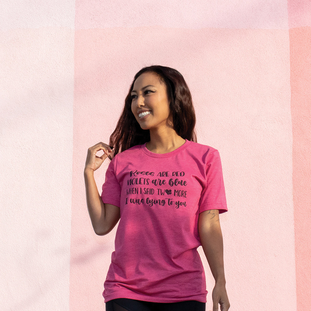Woman wearing a heather raspberry unisex crew t-shirt that says "Roses Are Red, Violets Are Blue, When I said Two More, I Was Lying To You" in black script.