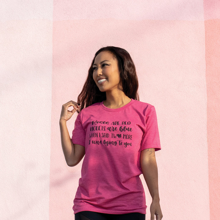 Woman wearing a heather raspberry unisex crew t-shirt that says "Roses Are Red, Violets Are Blue, When I said Two More, I Was Lying To You" in black script.