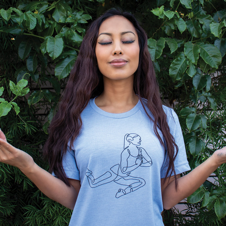 Woman wearing a heather blue t-shirt that has single line drawn woman doing the barre pretzel move.