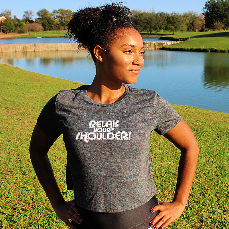 Woman wearing a heather gray cropped t-shirt that says "relax your shoulders"