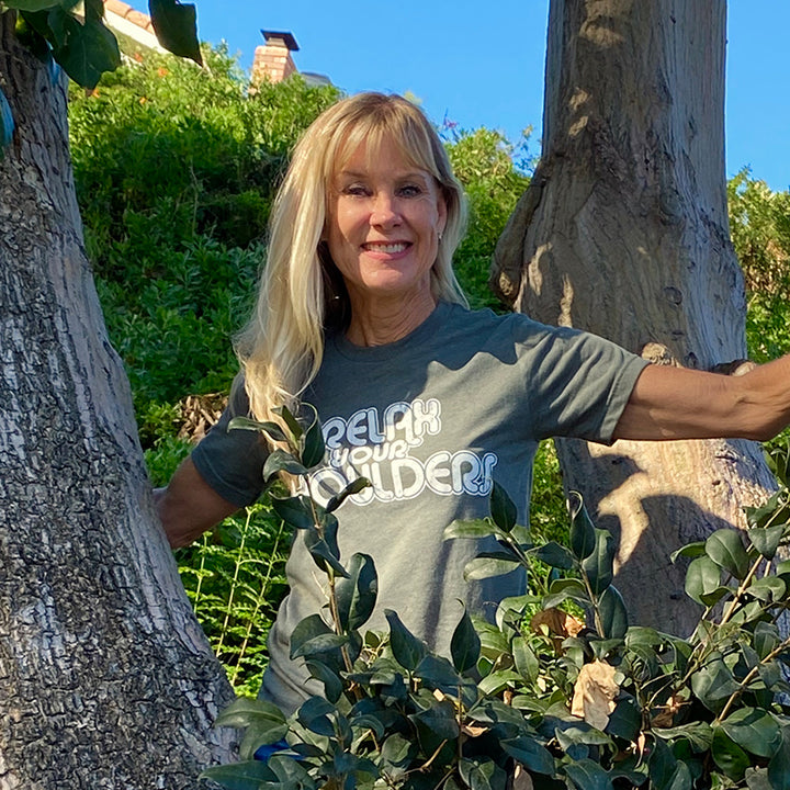 Woman wearing a heather military green shirt that says "relax your shoulders" in white retro text