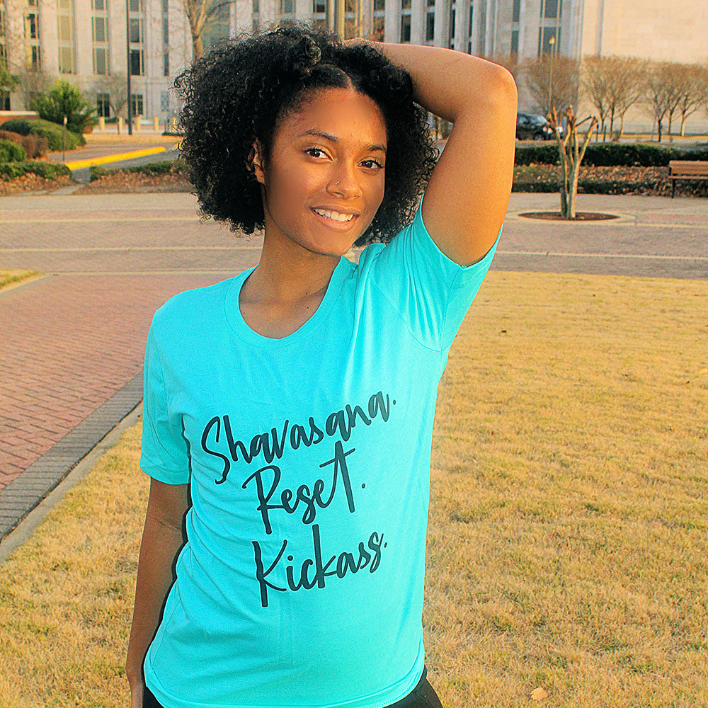 Woman wearing a unisex heather crew t-shirt that says "Shavasana Reset Kickass" in black text