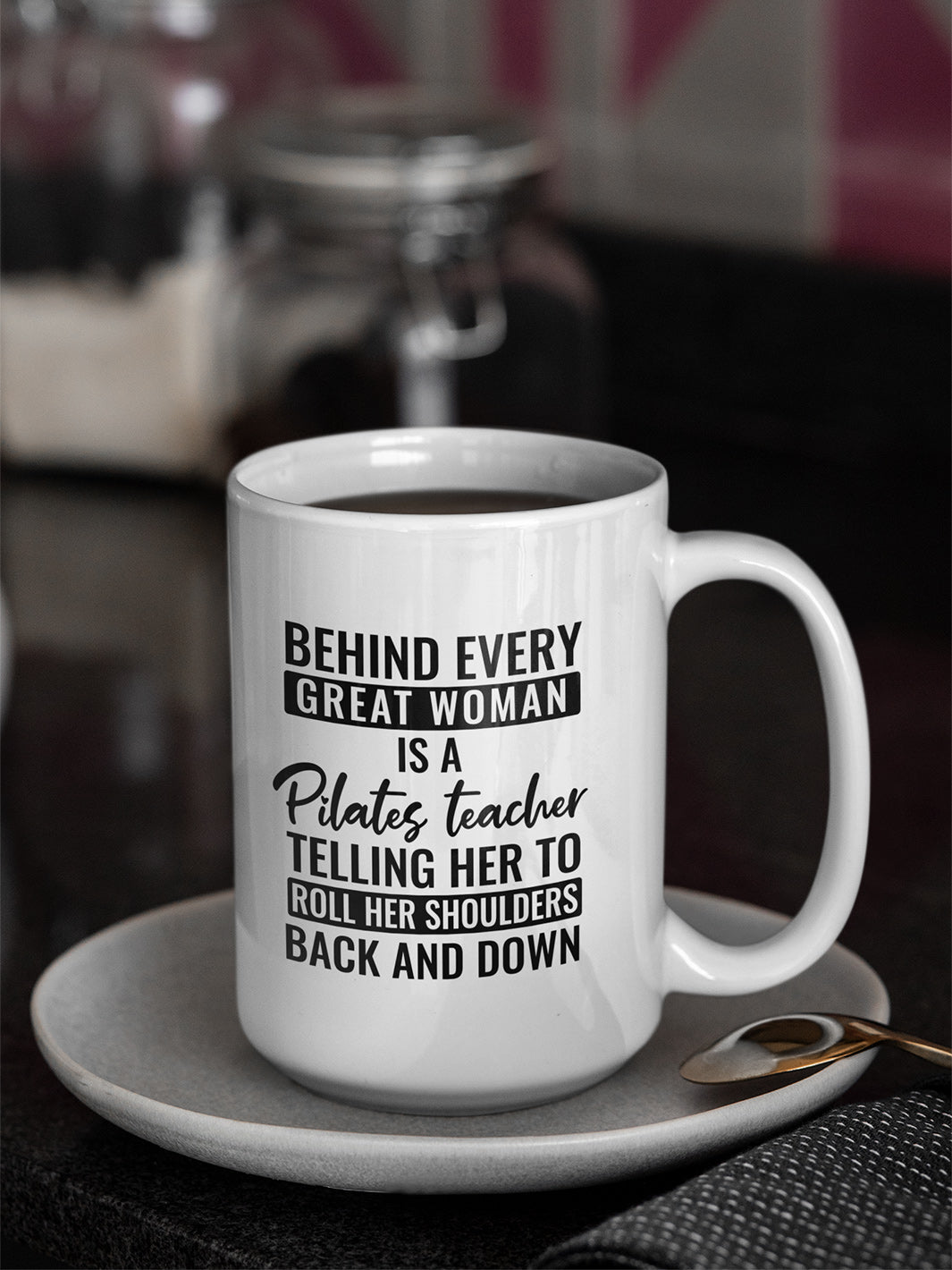 15 oz coffee mug that says "Behind Every Great Woman is A Pilates Teacher telling her to roll her shoulders back and down"