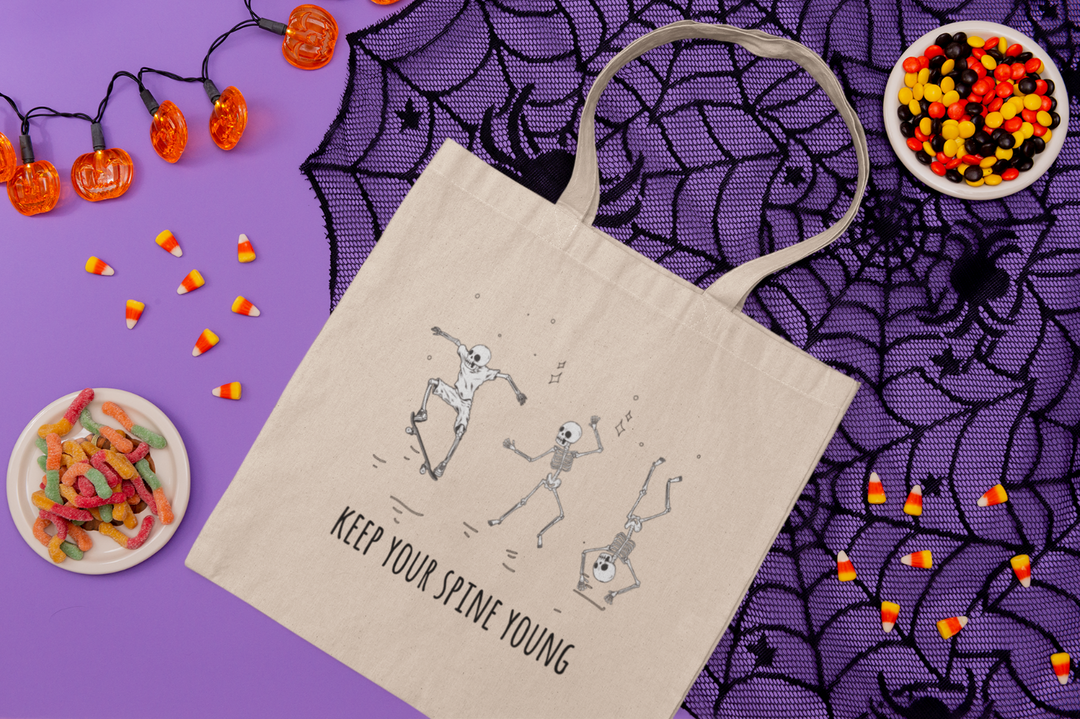 Canvas bag on halloween background that says "Spine Young" with three dancing skeletons 