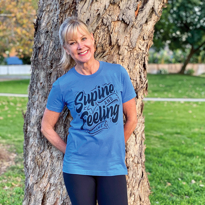 Woman wearing a blue t-shirt that says "supine and feeling fine" in black text