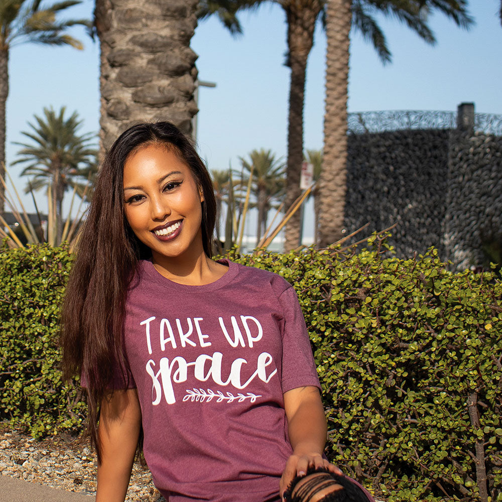 Woman wearing a maroon t-shirt that says "Take Up Space" in white writing