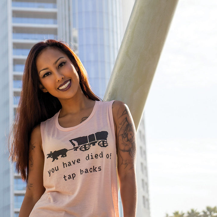 Woman wearing a women's cut peach muscle tank top that says you have died of tap backs under an old school Oregon Trail Covered Wagon in black text