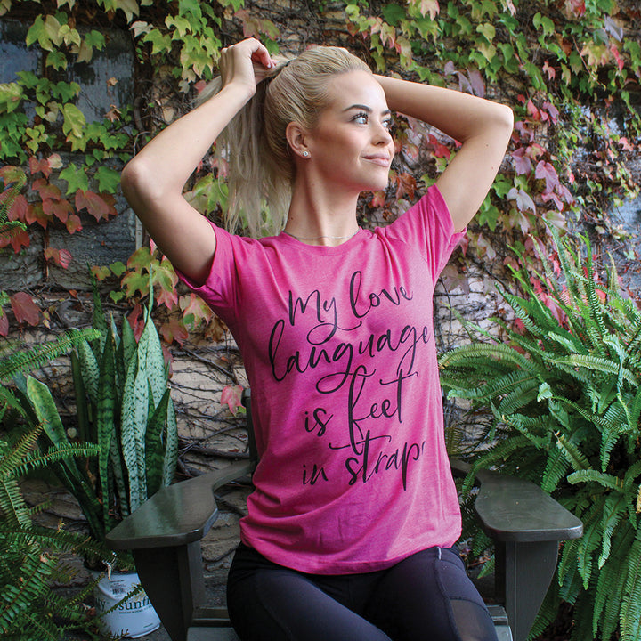Woman wearing a heather raspberry unisex crewneck t-shirt that says "My Love Language Is Feet In Straps" in black script