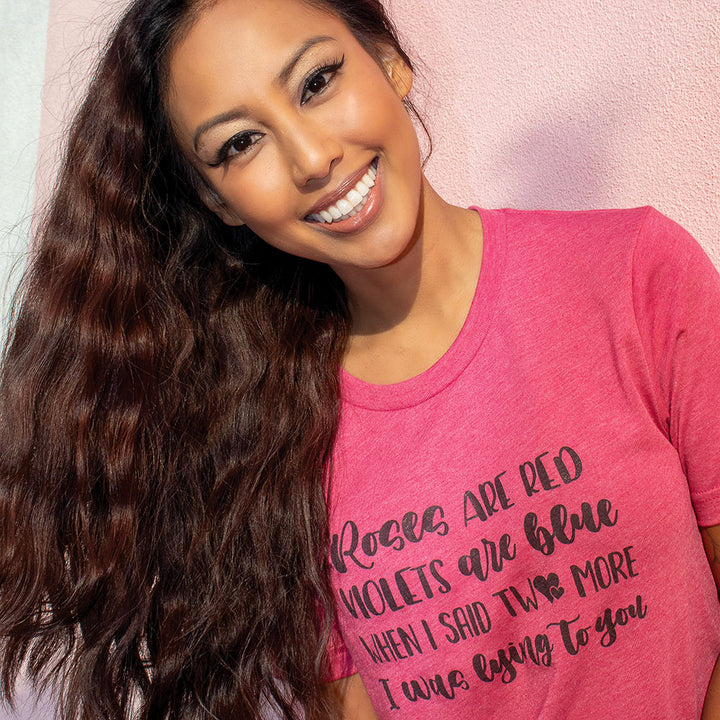 Woman wearing a heather raspberry unisex crew t-shirt that says "Roses Are Red, Violets Are Blue, When I said Two More, I Was Lying To You" in black script.