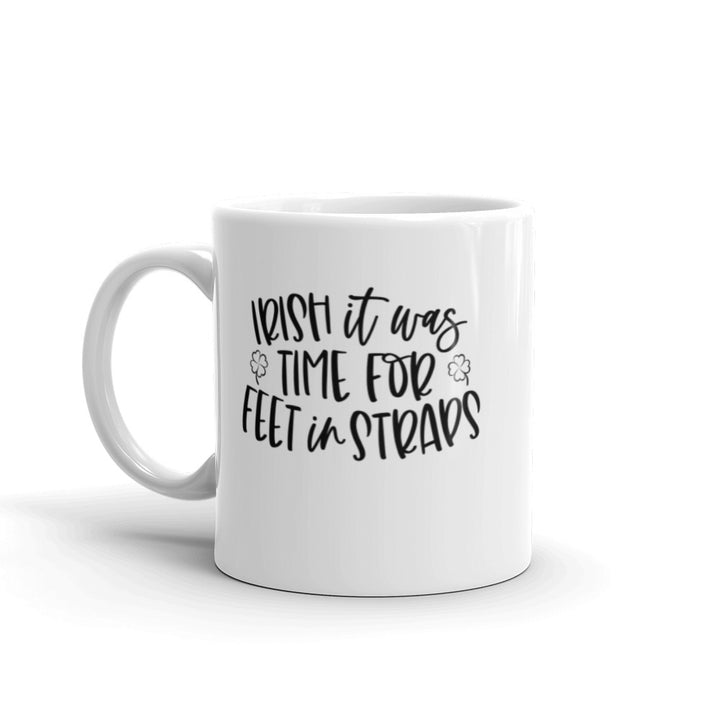 11 oz white coffee mug that says "Irish It Was Time For Feet In Straps" in black text. There are two black outline of 4 leaf clover on the front of the mug.