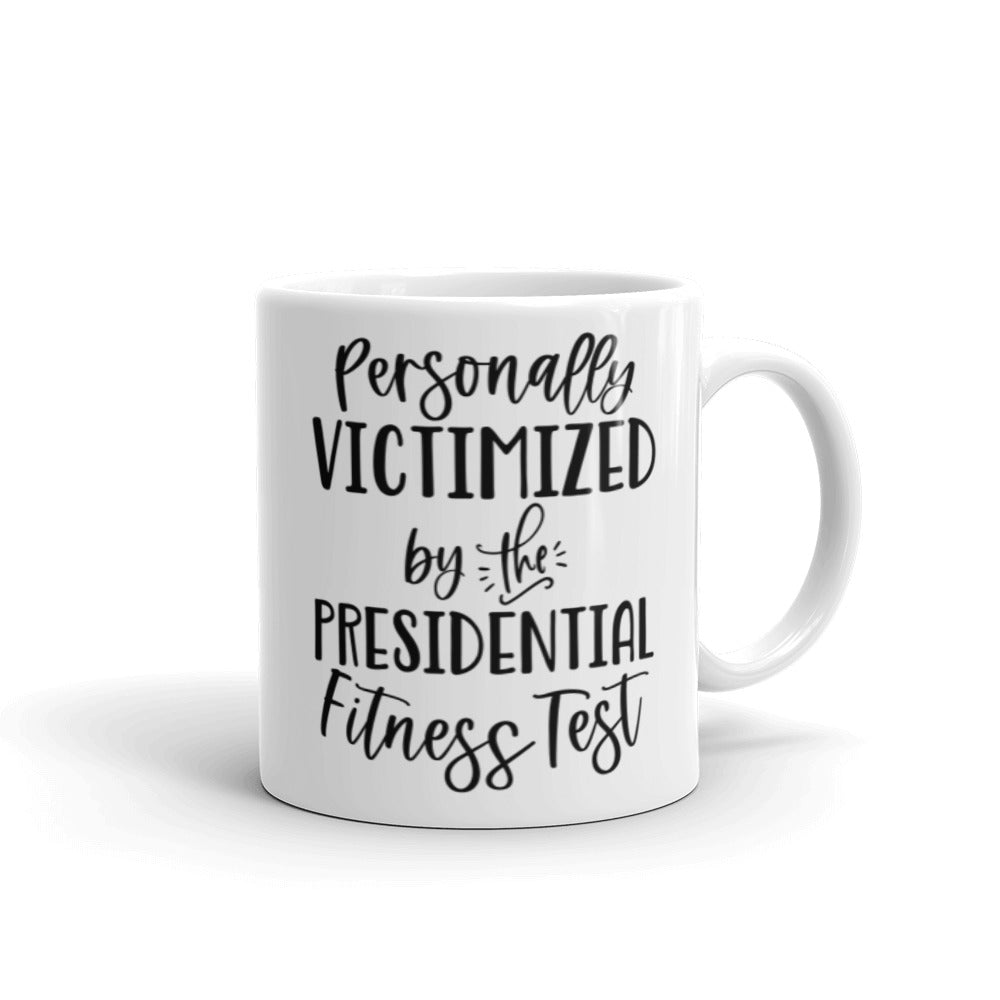 11 oz white ceramic mug that says "Personally victimized by the presidential fitness test"