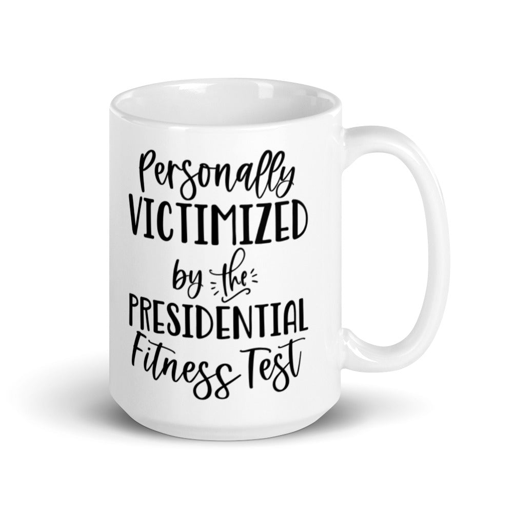15 oz white ceramic mug that says "Personally victimized by the presidential fitness test"